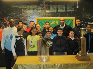 Youths and workers, most from the Mission Hill Youth Connection, pose with the Red Sox World Series trophy and the Mission Hill Little League championship trophy during an event Jan. 29 at the Tobin Community Center on Tremont Street. Hundreds of kids got their photos taken with the trophies. Pictured here are (from left): youth worker Charles Davis, Rosaury Mora, Raul Delarosa, Xavier Oller, William Battista, Selena Taylor, Debra Delarosa, Jayandy Tejeda, Will Gonzalez, Hector Galarza Jr., Katria Colon, Joandy Tejeda, Tobin Center Director John Jackson, Jeffrey Oller, Brian Mora and Jesse Smith. (Photo by Richard Rouse)